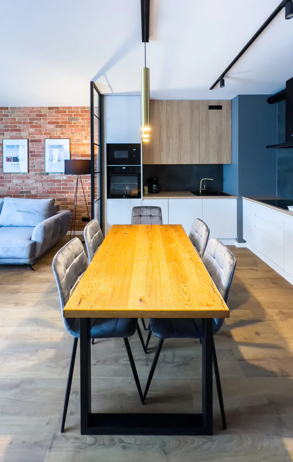 Apartament na DOKI 22F — drewniany stół na sześć osób, w tle widok na salon z cegłą