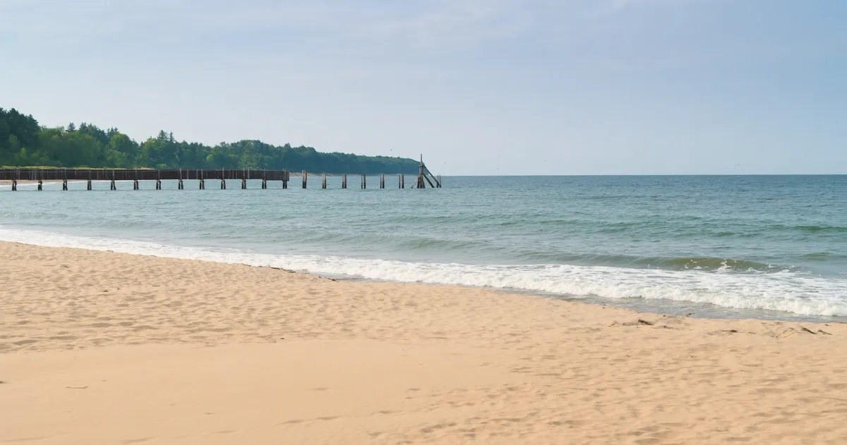 Piaszczysta plaża bałtycka wczesnym rankiem, w oddali zarys drewnianego molo
